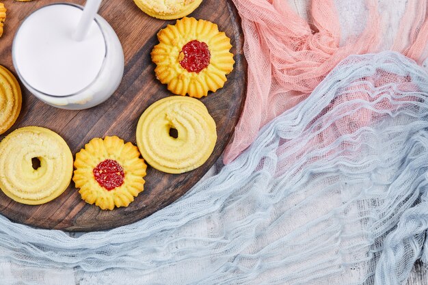 Biscuits assortis et un pot de lait sur une plaque en bois avec des nappes.