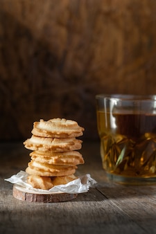 Biscuits au beurre empilés et un verre de thé sur fond de table en bois, photo verticale.