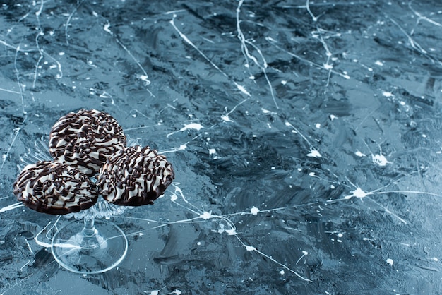 Biscuits au chocolat sur un socle en verre, sur la table bleue.