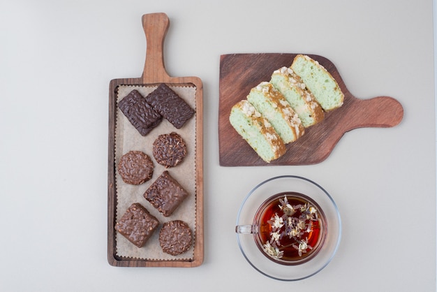 Biscuits au chocolat, tranches de gâteau à la pistache et verre de thé sur une surface blanche.