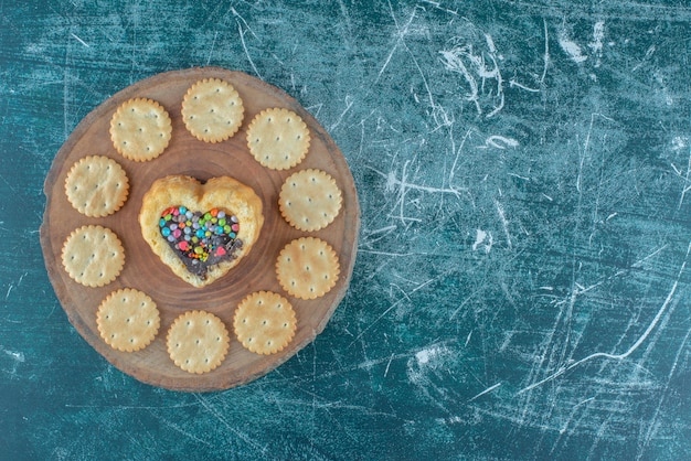 Photo gratuite biscuits autour d'un gâteau en forme de coeur sur une planche sur fond bleu. photo de haute qualité