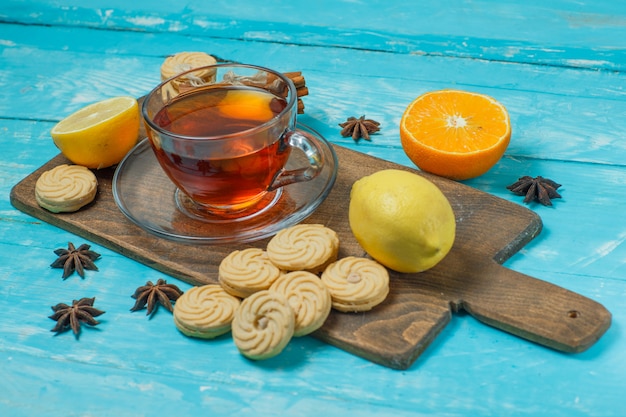 Biscuits aux épices, thé, citron, orange sur bleu et planche à découper, vue grand angle.