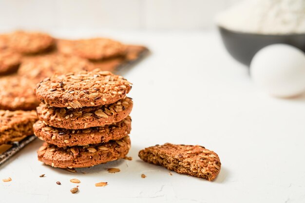 Biscuits à l'avoine avec graines de lin et de sésame sur fond blanc. Oeufs, farine - ingrédients pour faire des biscuits, recette de cuisson. Mise au point sélective sur les biscuits cuits au four, petit-déjeuner sain. Pâtisseries festives