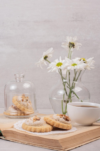 Biscuits à l'avoine, une tasse et des marguerites sur le livre.