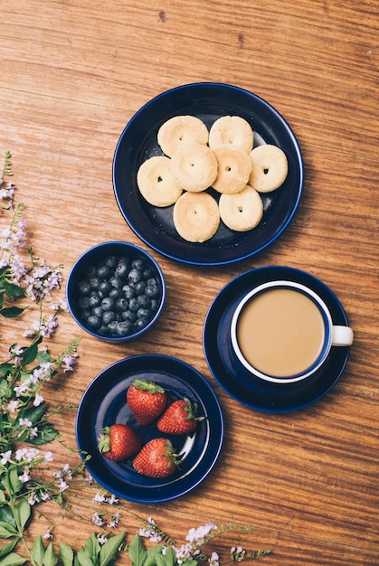 Photo gratuite biscuits cuits au four; tasse à café; myrtille et fraise à fleurs roses sur fond en bois