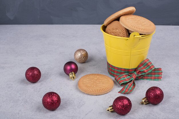 Biscuits dans un seau décoré de corde et boules de Noël sur table blanche.