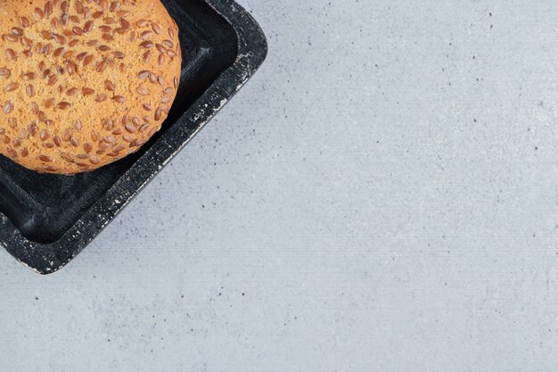 Biscuits enrobés de sésame sur un plateau noir sur fond de marbre.