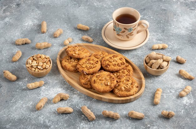 Biscuits faits maison avec des arachides biologiques et du miel sur une planche de bois avec une tasse de thé.