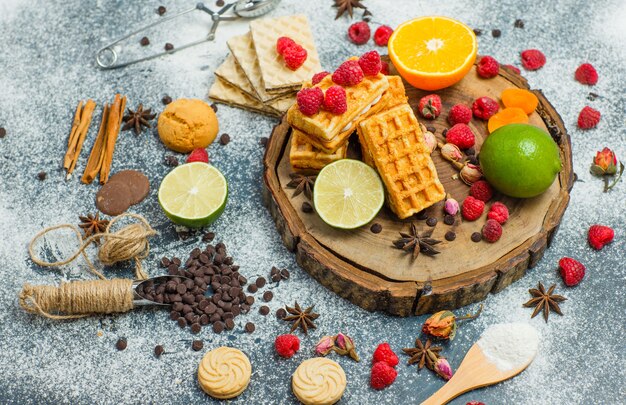 Biscuits à la farine, herbes, fruits, épices, choco, passoire à plat sur planche de bois et fond de stuc