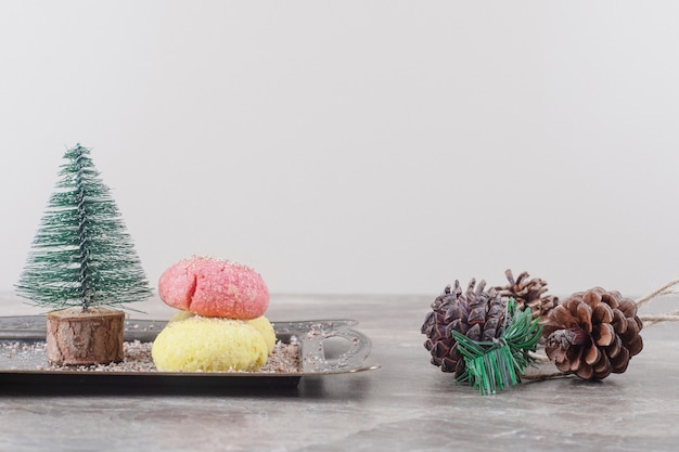 Biscuits, et une figurine d'arbre sur un plateau à côté de pommes de pin sur marbre