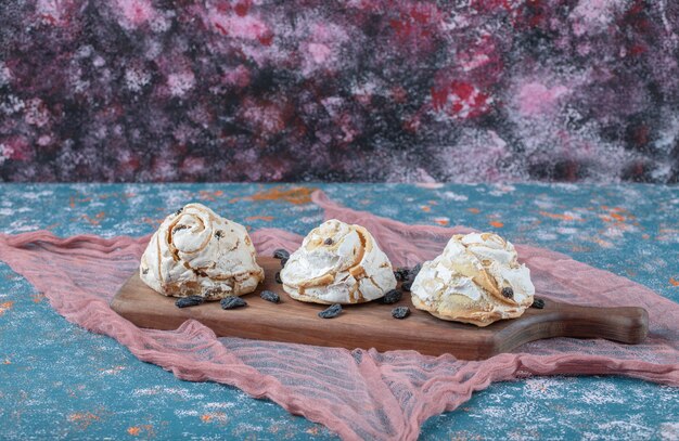 Biscuits de meringue blanche aux raisins secs noirs sur une planche de bois.