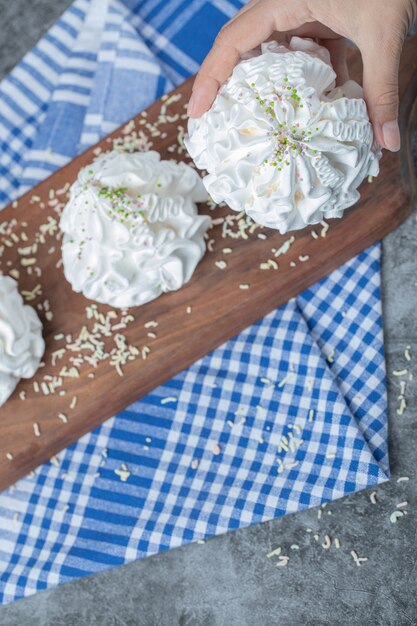 Biscuits à la meringue blanche avec de la poudre de noix de coco sur une planche de bois sur la serviette bleue.