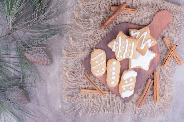 Biscuits en pain d'épice en forme d'étoile et ovale avec des bâtons de cannelle sur un plateau en bois.