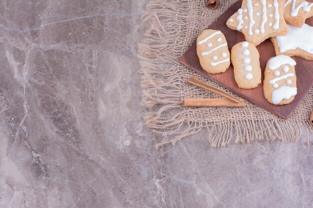 Biscuits en pain d'épice en forme d'étoile et ovale avec des bâtons de cannelle sur un plateau en bois.