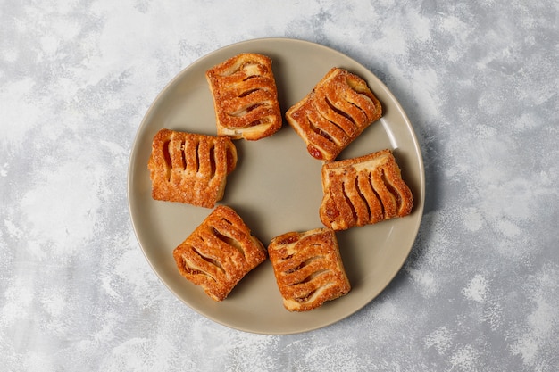 Biscuits de pâte feuilletée remplis de confiture de pommes et de pommes rouges fraîches sur du béton léger