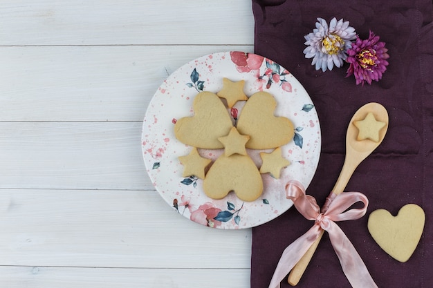 Biscuits à plat dans une assiette et une cuillère en bois avec des fleurs sur fond en bois et textile. horizontal