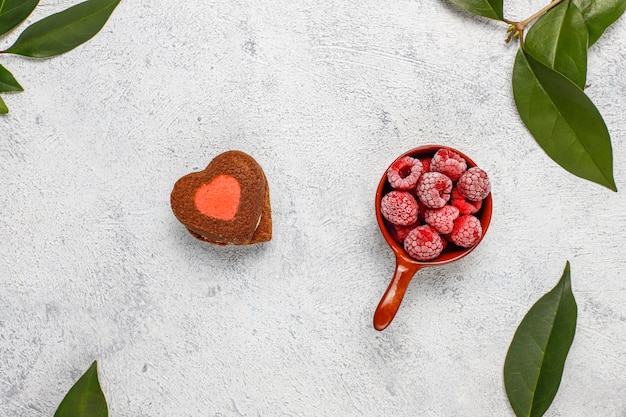 Biscuits de Saint Valentin en forme de coeur avec des framboises surgelées sur fond clair