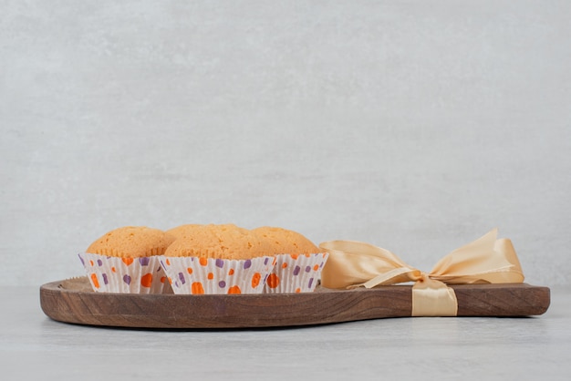 Biscuits sucrés à la crème sur une plaque en bois décorée de ruban.