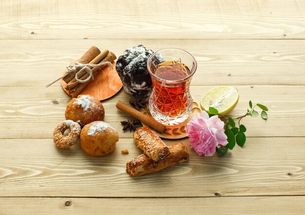 Biscuits avec un verre de thé, des bâtons de cannelle, des fleurs, du citron, des clous de girofle sur une surface en bois, high angle view.