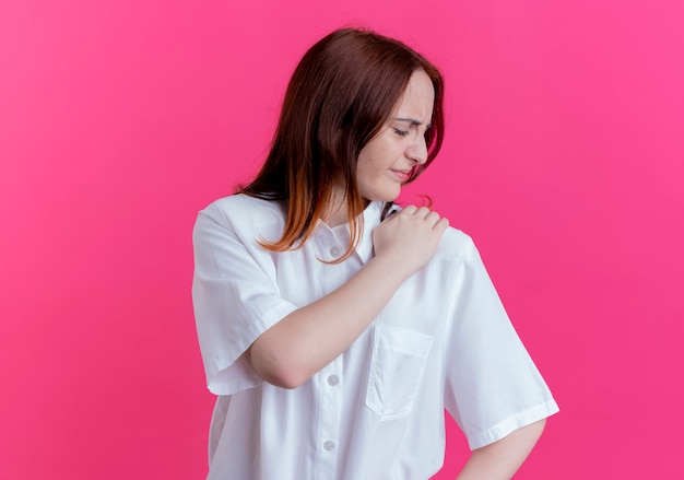 Blessé jeune fille rousse a saisi l'épaule isolé sur un mur rose