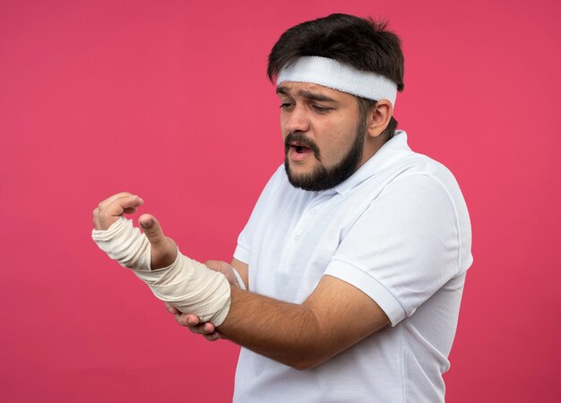 Blessé jeune homme sportif portant un bandeau et un bracelet avec poignet enveloppé de bandage a attrapé le poignet douloureux