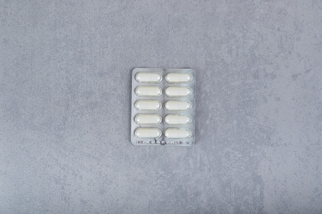 Un blister avec des pilules blanches sur une surface grise