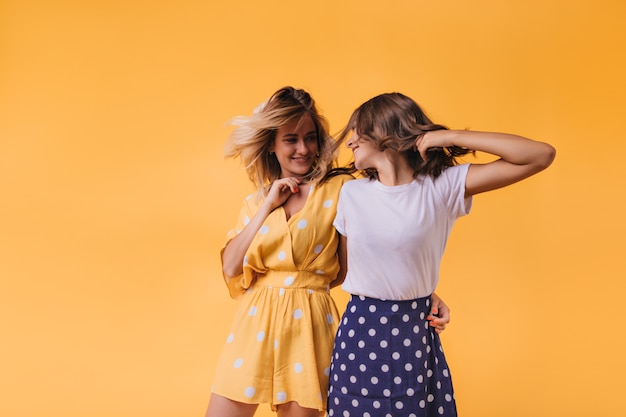 Blithesome Jeune Femme En Tenue Jaune Regardant Un Ami Avec Le Sourire. Joyeuses Soeurs Caucasiennes Se Détendre Sur L'orange.