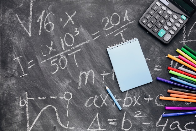 Photo gratuite bloc-notes et calculatrice avec des feutres disposés sur un tableau écrit