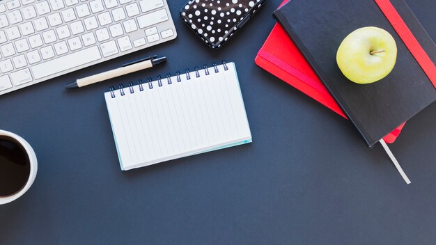 Bloc-notes et clavier près de tasse à café et pomme