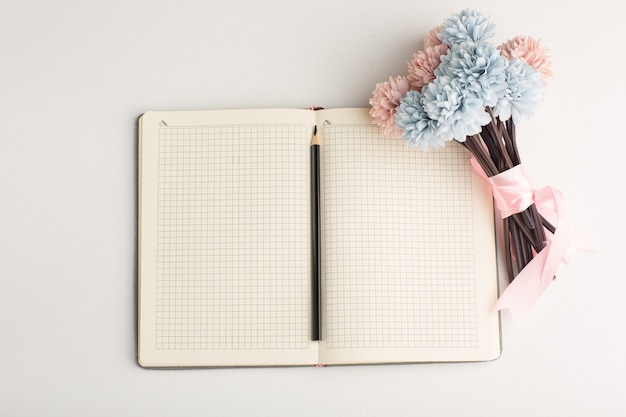 Photo gratuite bloc-notes ouvert vue de dessus avec fleur et crayon sur surface blanche