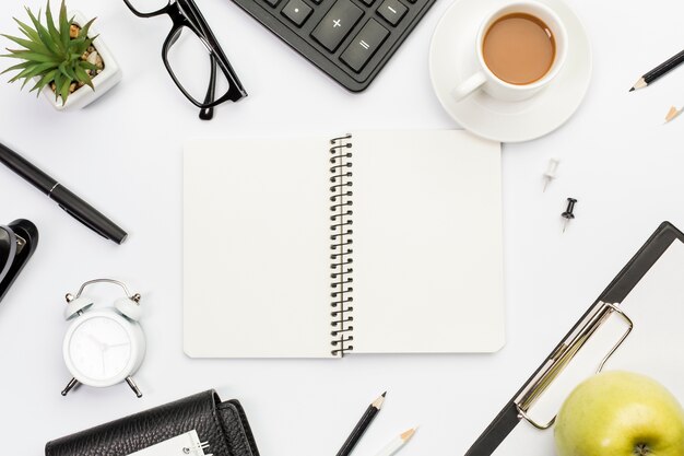 Bloc-notes à spirale entouré de papeterie, de pomme et de café sur un bureau blanc