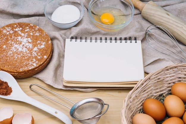 Bloc-notes en spirale avec des ingrédients et des outils pour préparer un gâteau