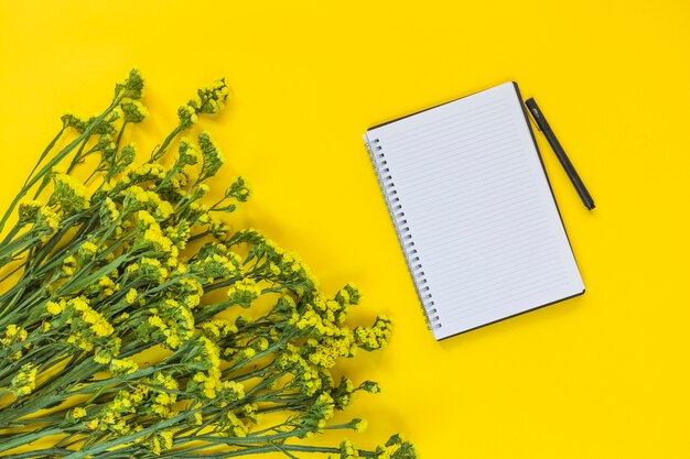 Photo gratuite bloc-notes en spirale et stylo près du bouquet de fleurs fraîches sur fond jaune