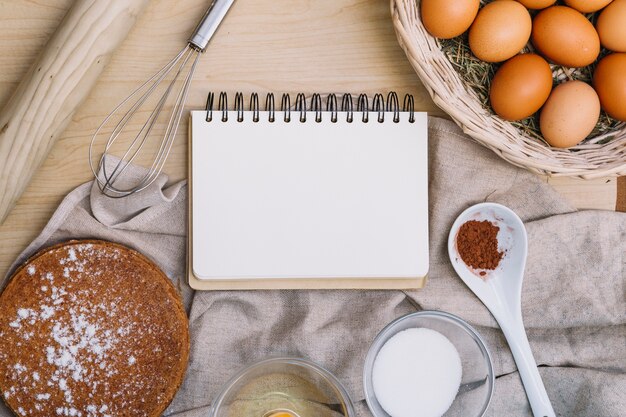 Bloc-notes en spirale vierge avec divers ingrédients de gâteau de cuisson sur la table