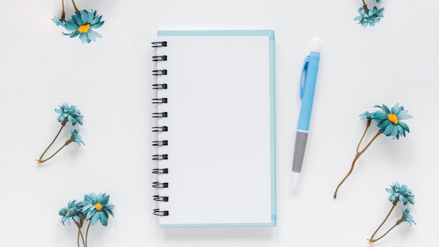 Photo gratuite bloc-notes et stylo près de fleurs de camomille bleues