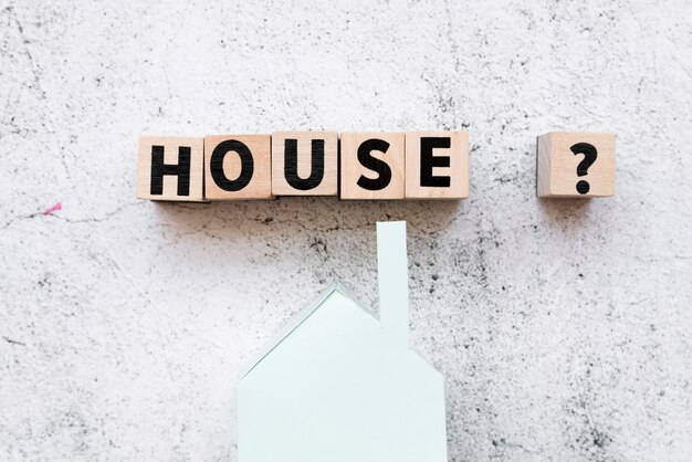 Blocs de texte de maison arrangés avec le signe de la question sur le modèle de maison en papier sur fond de béton