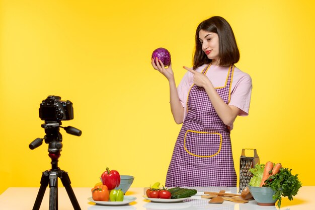 Blogueur culinaire jolie jolie fille en tablier rose enregistrant une vidéo pour les médias sociaux montrant un oignon