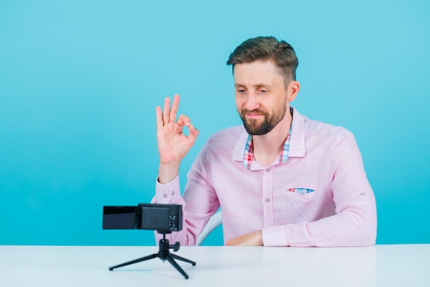 Un blogueur montre un geste correct à sa mini caméra sur fond bleu