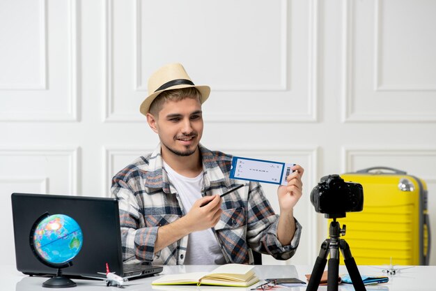 Blogueur de voyage portant un chapeau de paille jeune beau mec enregistrant un vlog de voyage sur une caméra tenant un billet