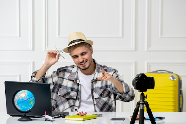 Photo gratuite blogueur de voyage portant un chapeau de paille jeune beau mec enregistrant un vlog de voyage devant une caméra volant à l'étranger