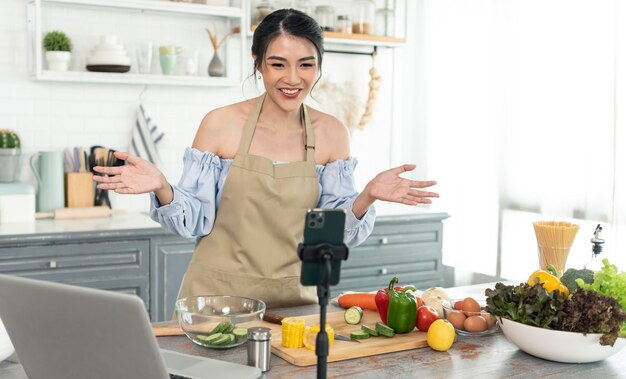 Une blogueuse asiatique cuisine une salade devant la caméra d'un smartphone lors de l'enregistrement d'une vidéo vlog