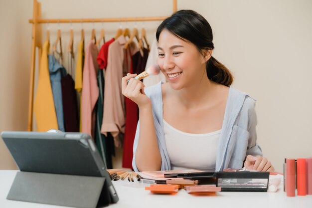 Une blogueuse beauté présente des produits de beauté assis devant une tablette pour enregistrer une vidéo.