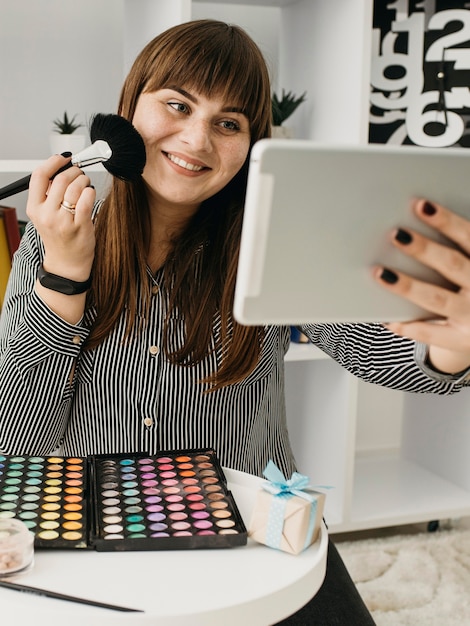 Photo gratuite blogueuse de maquillage féminin smiley avec streaming avec tablette à la maison