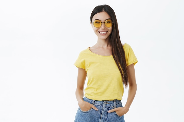 Blogueuse de mode féminine élégante, affirmée et confiante, dans des lunettes de soleil jaunes à la mode, tenant la main dans les poches