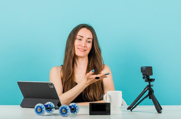 Une blogueuse souriante pose à la caméra en levant la main sur fond bleu