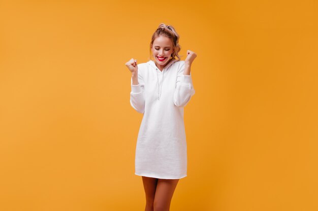 Une blonde agréable et amicale en robe de style urbain tient ses mains dans les poings et rit