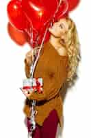 Photo gratuite blonde belle femme en pull confortable tenant présent et ballons