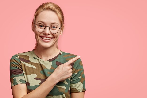 Blonde belle femme avec un sourire positif, montre des dents blanches, indique de côté