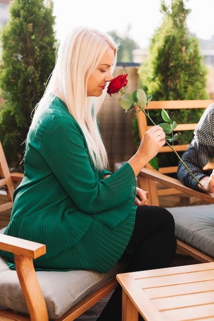 Blonde belle jeune femme sentant la rose rouge