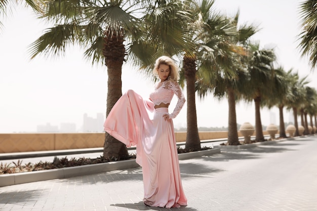 Blonde galbée au bord de la mer à Dubaï, palmiers, robes chaudes et magnifiques, tir de mode de mode de vie ensoleillé d'été, agitant la robe du vent, calme et se détendre près de la piscine, coiffure, maquillage